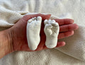 Newborn handprint kit featuring life-sized baby hand and foot casts in a person's hand.